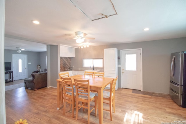 dining area featuring sink, a fireplace, ceiling fan, and light wood-type flooring