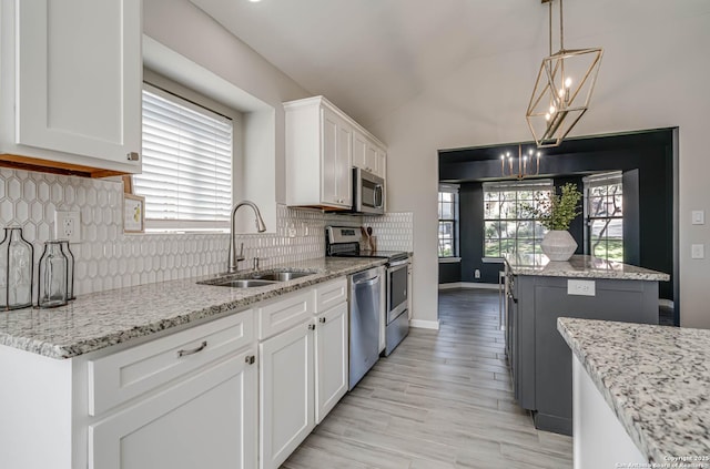 kitchen featuring sink, appliances with stainless steel finishes, white cabinetry, hanging light fixtures, and light stone countertops