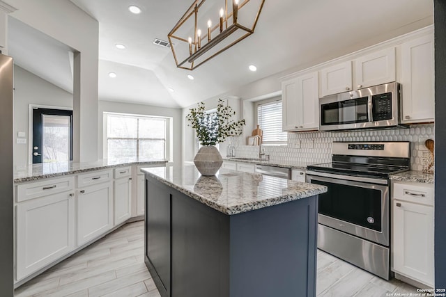 kitchen featuring lofted ceiling, white cabinetry, stainless steel appliances, a kitchen island, and decorative light fixtures