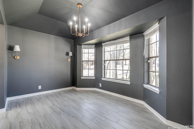 empty room featuring vaulted ceiling, a healthy amount of sunlight, a notable chandelier, and light hardwood / wood-style floors