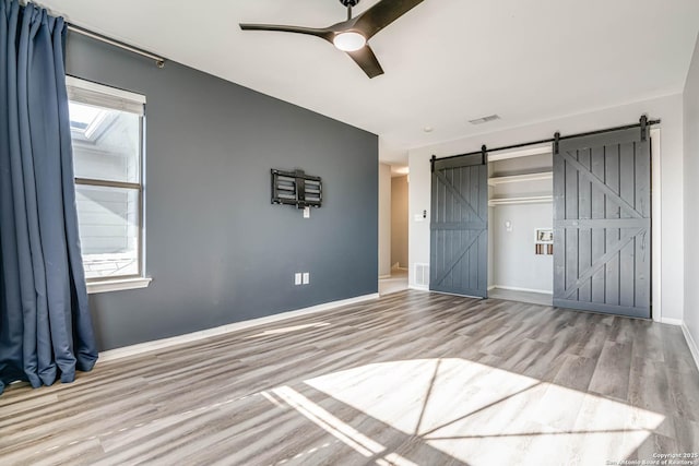 unfurnished bedroom featuring light hardwood / wood-style floors, a barn door, and ceiling fan