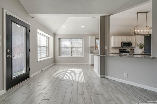 kitchen with vaulted ceiling, tasteful backsplash, white cabinetry, light stone counters, and stainless steel appliances