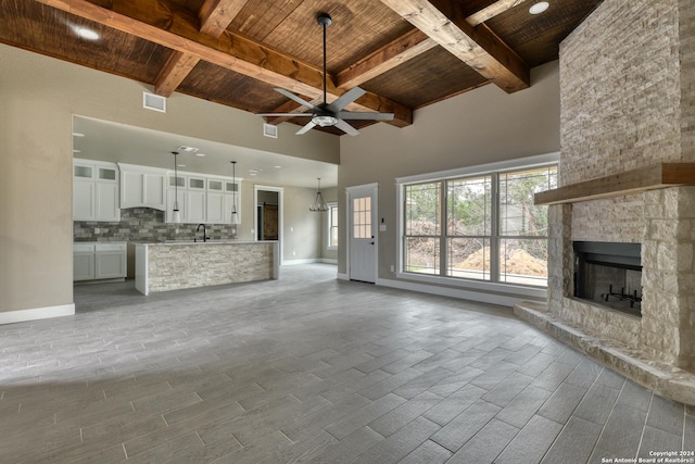 unfurnished living room with wood ceiling, ceiling fan, a stone fireplace, and beam ceiling