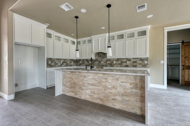 kitchen with a barn door, a kitchen island with sink, white cabinets, and light stone counters