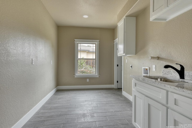 kitchen featuring white cabinetry, sink, light stone counters, and a textured ceiling