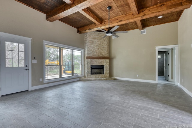 unfurnished living room with ceiling fan, beam ceiling, a towering ceiling, a fireplace, and wooden ceiling