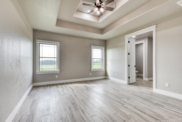 unfurnished room with ceiling fan, a raised ceiling, and light wood-type flooring