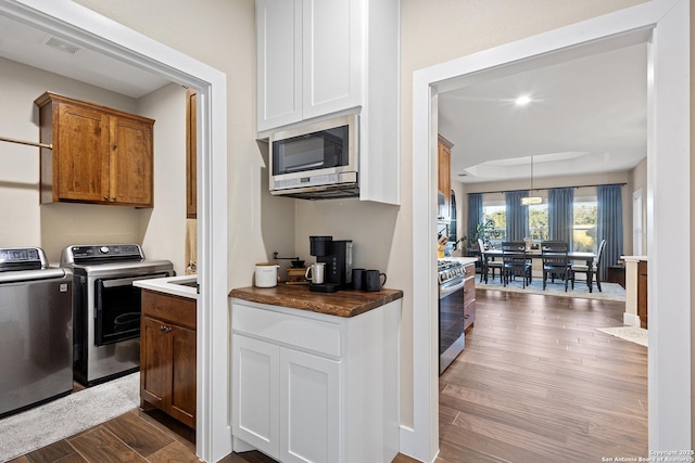 kitchen with appliances with stainless steel finishes, washer and dryer, decorative light fixtures, white cabinetry, and light wood-type flooring