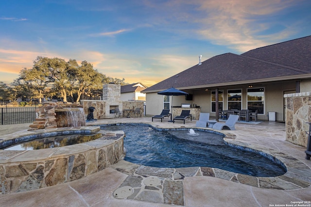 pool at dusk with pool water feature, a patio, an outdoor stone fireplace, and an in ground hot tub