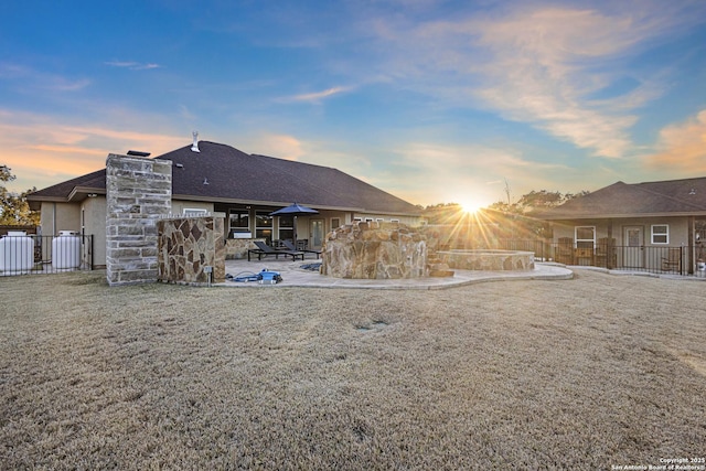 back house at dusk featuring a patio and a lawn