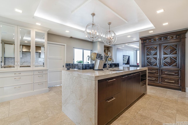 kitchen with white cabinetry, an island with sink, a raised ceiling, and sink