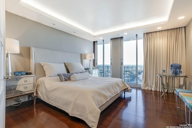 bedroom with dark hardwood / wood-style flooring, a wall of windows, a raised ceiling, and access to outside