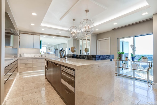 kitchen with sink, a raised ceiling, light stone countertops, a kitchen island with sink, and white cabinets