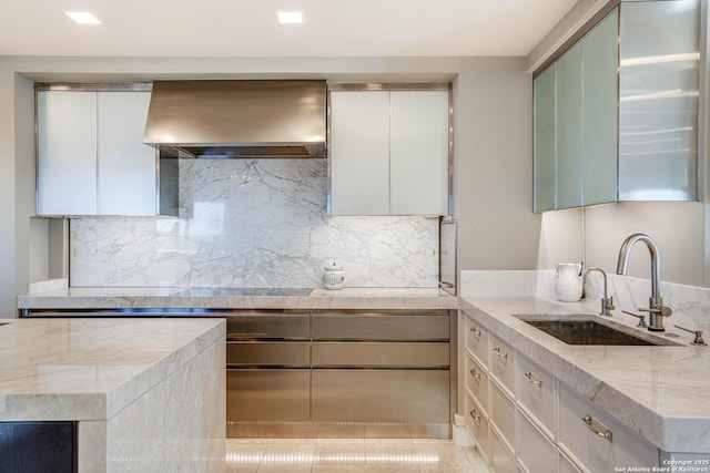 kitchen with sink, premium range hood, white cabinetry, backsplash, and light stone countertops