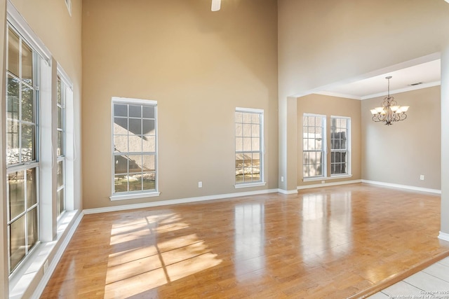 unfurnished room featuring plenty of natural light, a chandelier, light hardwood / wood-style flooring, and a high ceiling