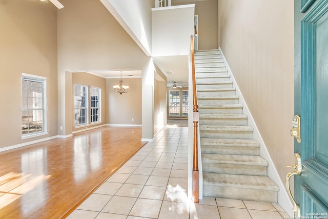 tiled entrance foyer featuring a towering ceiling and ceiling fan with notable chandelier