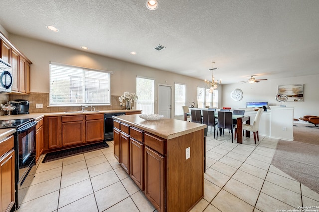 kitchen featuring pendant lighting, light tile patterned floors, backsplash, a center island, and black appliances