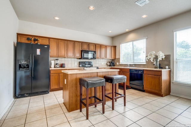 kitchen featuring light tile patterned floors, sink, a kitchen island, black appliances, and a kitchen bar