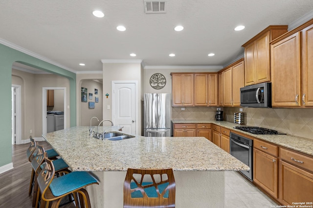 kitchen featuring washing machine and clothes dryer, sink, a kitchen breakfast bar, stainless steel appliances, and a kitchen island with sink