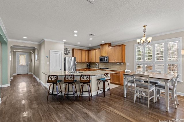 kitchen with appliances with stainless steel finishes, decorative light fixtures, an island with sink, a kitchen bar, and crown molding