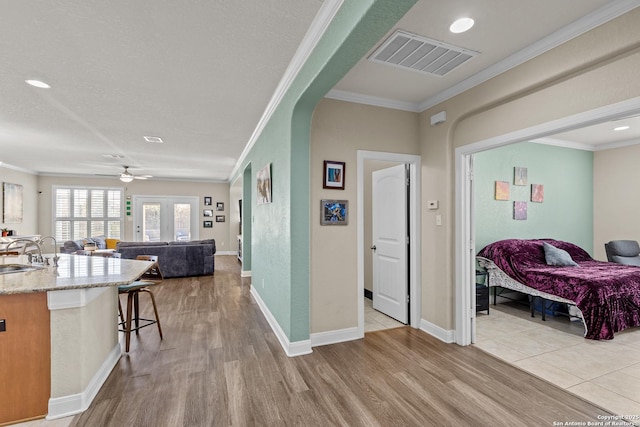 interior space featuring sink, a kitchen breakfast bar, light stone counters, crown molding, and light wood-type flooring