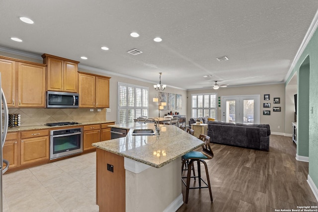 kitchen with sink, tasteful backsplash, a center island with sink, ornamental molding, and stainless steel appliances