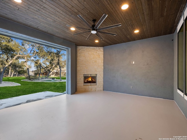 interior space featuring wood ceiling, ceiling fan, concrete floors, and an outdoor stone fireplace