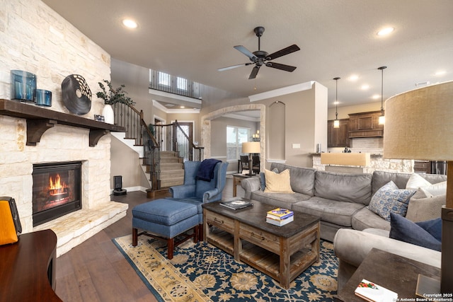 living room featuring dark wood-type flooring, a textured ceiling, ornamental molding, ceiling fan, and a fireplace