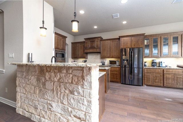 kitchen with dark hardwood / wood-style floors, decorative light fixtures, kitchen peninsula, stainless steel appliances, and light stone countertops