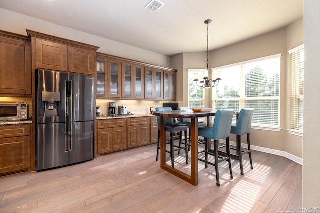 kitchen featuring hanging light fixtures, light stone counters, stainless steel fridge with ice dispenser, a chandelier, and light wood-type flooring