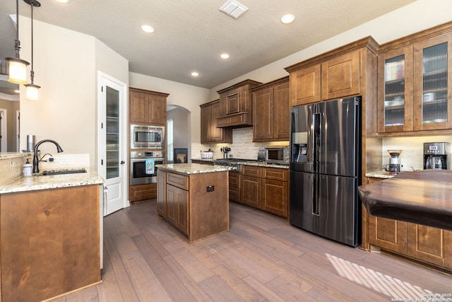 kitchen featuring sink, tasteful backsplash, light stone counters, hanging light fixtures, and stainless steel appliances