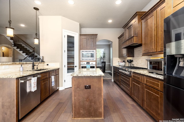 kitchen featuring pendant lighting, appliances with stainless steel finishes, a center island, decorative backsplash, and kitchen peninsula