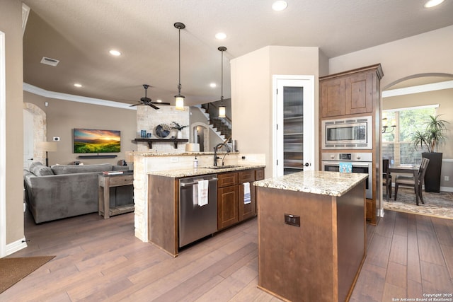 kitchen featuring sink, stainless steel appliances, light stone countertops, decorative light fixtures, and kitchen peninsula