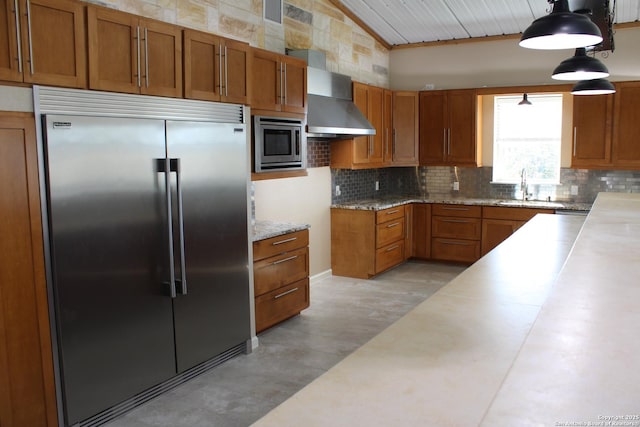 kitchen featuring sink, decorative backsplash, hanging light fixtures, built in appliances, and wall chimney range hood