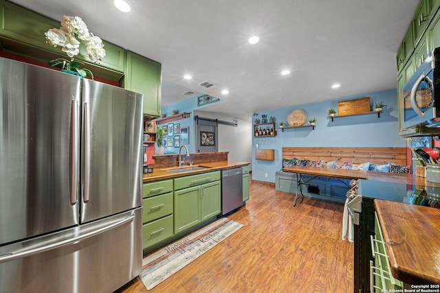 kitchen featuring wood counters, a barn door, green cabinetry, and appliances with stainless steel finishes