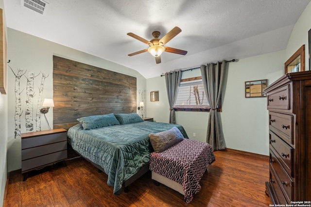 bedroom with dark wood-type flooring, wood walls, a textured ceiling, and vaulted ceiling