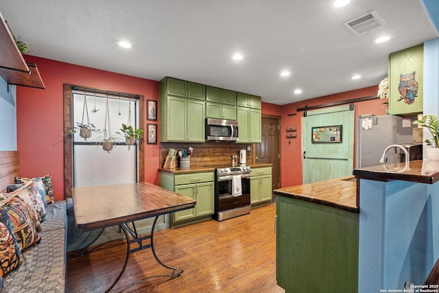 kitchen featuring appliances with stainless steel finishes, kitchen peninsula, green cabinets, a barn door, and light hardwood / wood-style floors