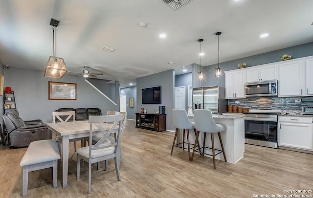 kitchen featuring stainless steel appliances, decorative light fixtures, light stone countertops, and a kitchen island with sink