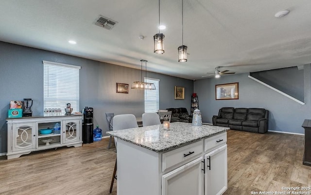 kitchen featuring a breakfast bar area, decorative light fixtures, a center island, light wood-type flooring, and white cabinets