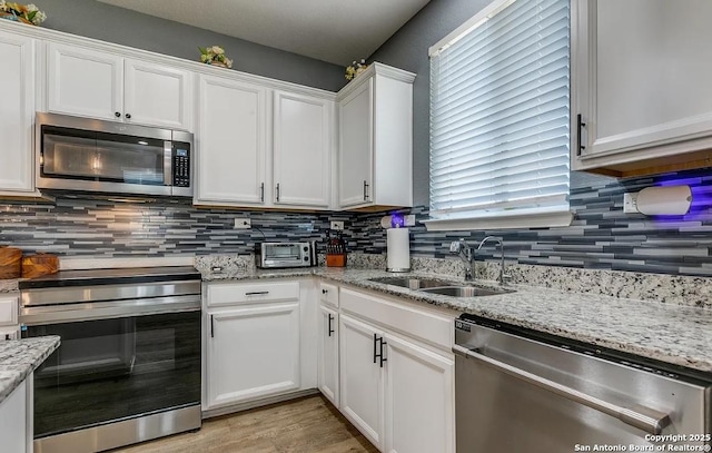 kitchen featuring sink, white cabinetry, stainless steel appliances, tasteful backsplash, and light stone countertops