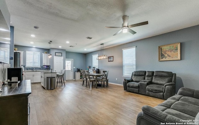 living room with ceiling fan, a textured ceiling, and light wood-type flooring