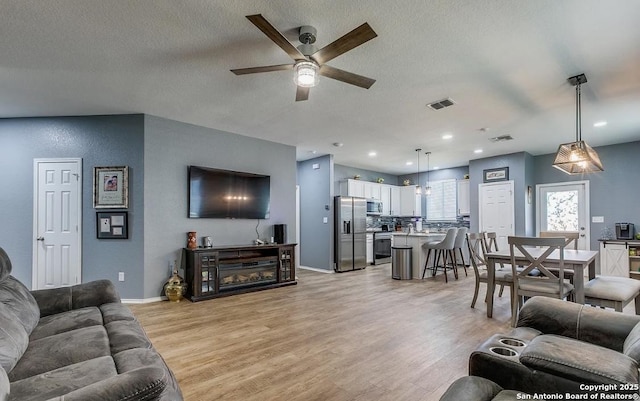 living room featuring ceiling fan, a textured ceiling, and light hardwood / wood-style floors