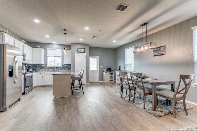 kitchen with appliances with stainless steel finishes, decorative light fixtures, white cabinetry, a kitchen bar, and a center island