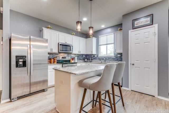 kitchen with decorative light fixtures, white cabinetry, a center island, light stone counters, and stainless steel appliances