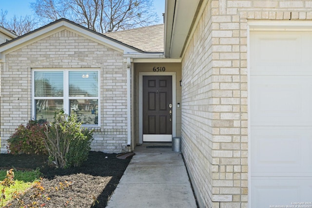 view of exterior entry featuring brick siding, roof with shingles, and an attached garage