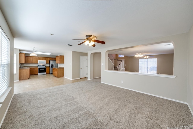 unfurnished living room with ceiling fan with notable chandelier, light colored carpet, sink, and a wealth of natural light