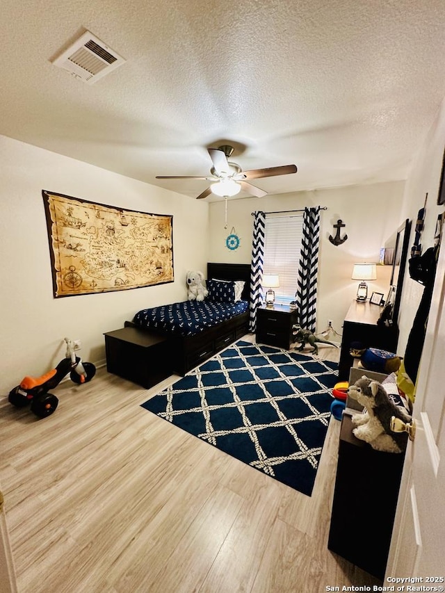 bedroom with a textured ceiling, wood-type flooring, and ceiling fan