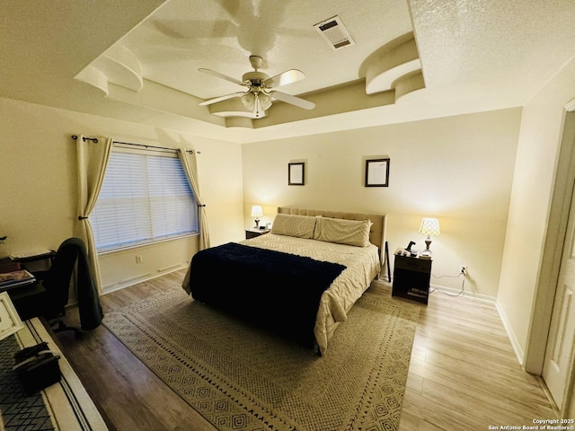 bedroom featuring a textured ceiling, light hardwood / wood-style flooring, a raised ceiling, and ceiling fan