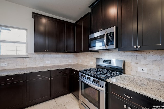 kitchen with stainless steel appliances, light stone countertops, dark brown cabinets, and light tile patterned floors