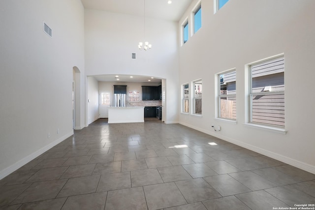 unfurnished living room with an inviting chandelier, a towering ceiling, and tile patterned flooring